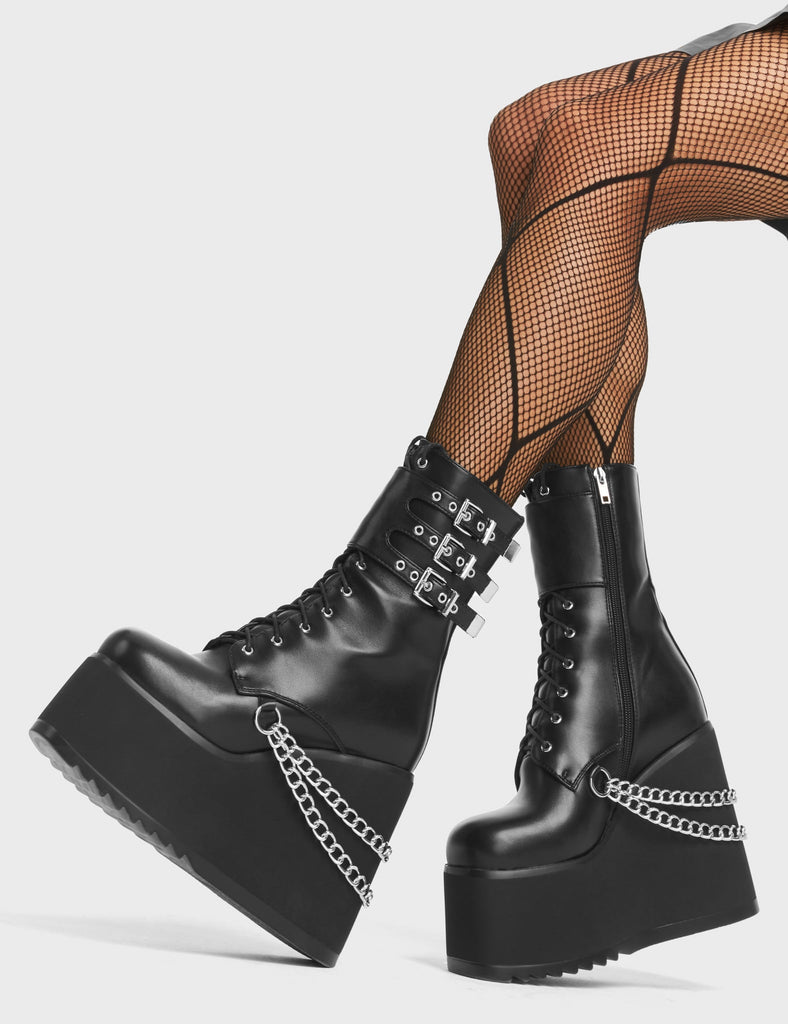 Dumb Love Chunky Platform Ankle Boots in Black Faux Leather. These chunky wedge boots feature a lace-up fastening, three adjustable straps above the ankle and silver chain detailing hanging around the heel. Made with eco-friendly materials and 100% cruelty-free