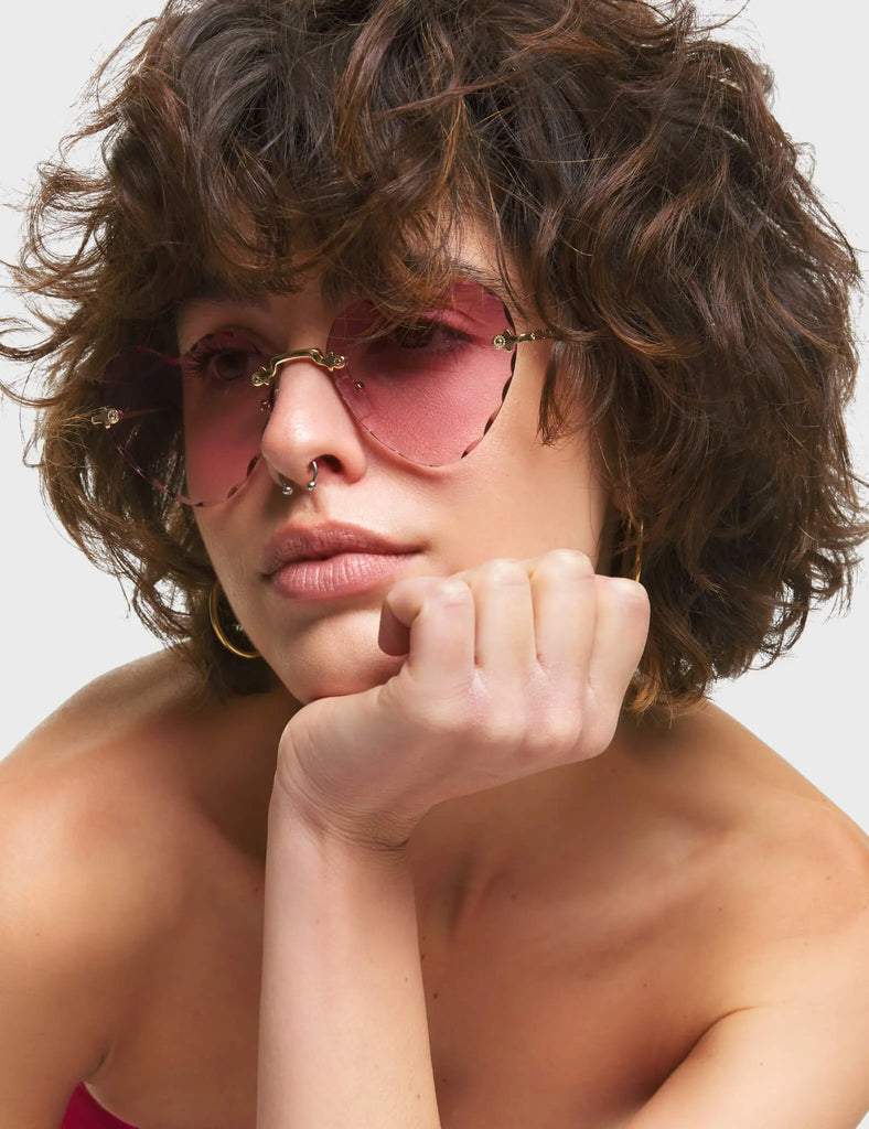 Eye Candy Heart Sunglasses. These Heart sunglasses feature antique style Gold arms, and a Pink tinted heart shaped lens.
