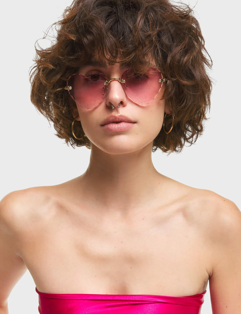 Eye Candy Heart Sunglasses. These Heart sunglasses feature antique style Gold arms, and a Pink tinted heart shaped lens.