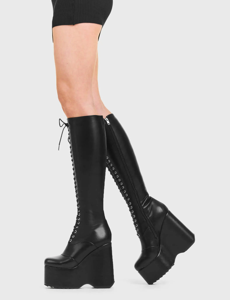 ICONIC Kiss CIty Chunky Platform Knee High Boots in Black faux leather. These platform boots feature a black lace up design with a platformed wedge. Made with eco-friendly materials and 100% cruelty-free, these platform boots are as ethical as they are chic. - Platform Height - Knee high length - Black lace up - Rounded toe - High Heel - 100% vegan SKU: LMF 3545 - BlackPU