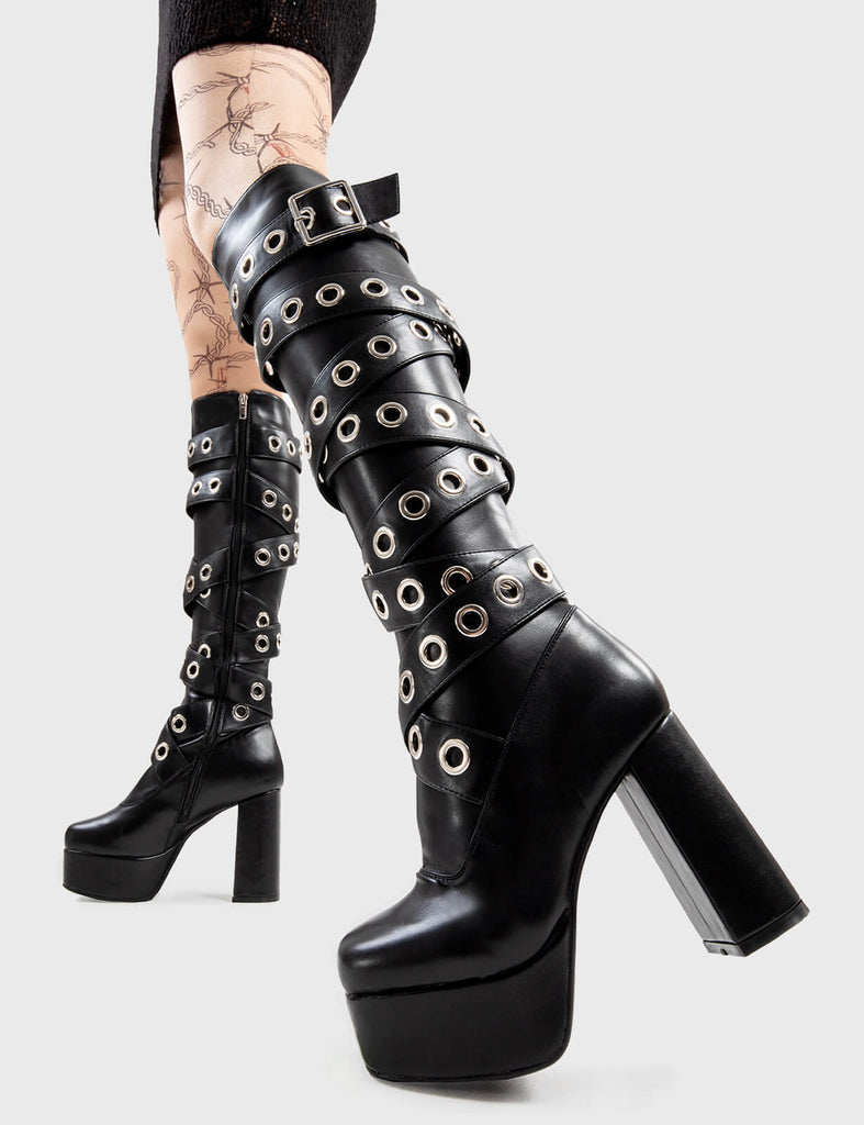 Sizzling Stompers Manhunt Platform Knee High Boots in Black faux . These platform boots feature a large eyelet design that twists up the boot, set new fashion trends with these iconic boots.Made with eco-friendly materials and 100% cruelty-free, these platform boots are as ethical as they are Iconic! - Platform Height - Heel Height - Black Zip - Knee high length - Silver eyelet and square shaped buckles - Platform sole - Round Toe - 100% vegan SKU: LMF 2820 - BlackPU