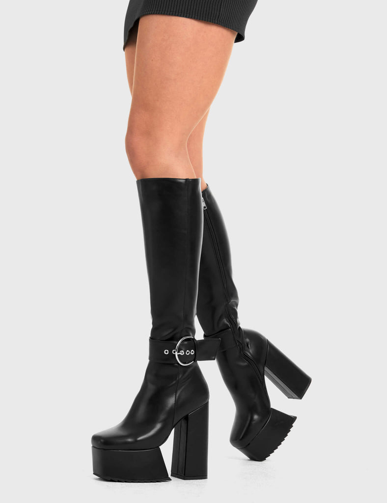 Not Your Basic Boots Power Over You Platform Knee High Boots in Black faux leather. These platform boots feature a minimalist design, with a strap around the ankle and a silver 'O' ring buckle, the perfect pair with any outfit. Made with eco-friendly materials and 100% cruelty-free - Platform Height - Heel Height - Black Zipper - Ankle strap and Silver buckle - Thigh length - Platform sole - Shark's teeth grip - High Heel - 100% vegan SKU: LMF 2880 - BlackPU