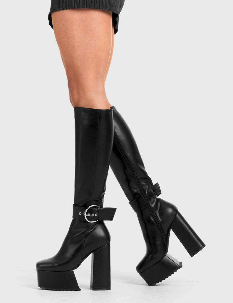 Not Your Basic Boots Power Over You Platform Knee High Boots in Black faux leather. These platform boots feature a minimalist design, with a strap around the ankle and a silver 'O' ring buckle, the perfect pair with any outfit. Made with eco-friendly materials and 100% cruelty-free - Platform Height - Heel Height - Black Zipper - Ankle strap and Silver buckle - Thigh length - Platform sole - Shark's teeth grip - High Heel - 100% vegan SKU: LMF 2880 - BlackPU