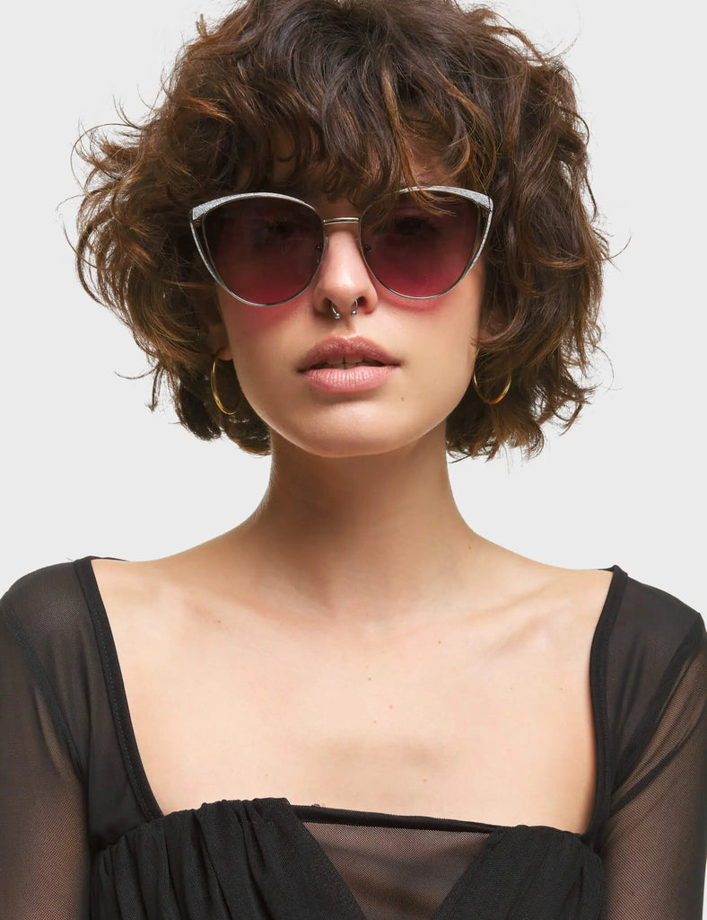 Rosa Cateye Sunglasses. These Cateye sunglasses feature a Silver frame with Silver Glitter eyebrows, and a dark Pink tinted lens.