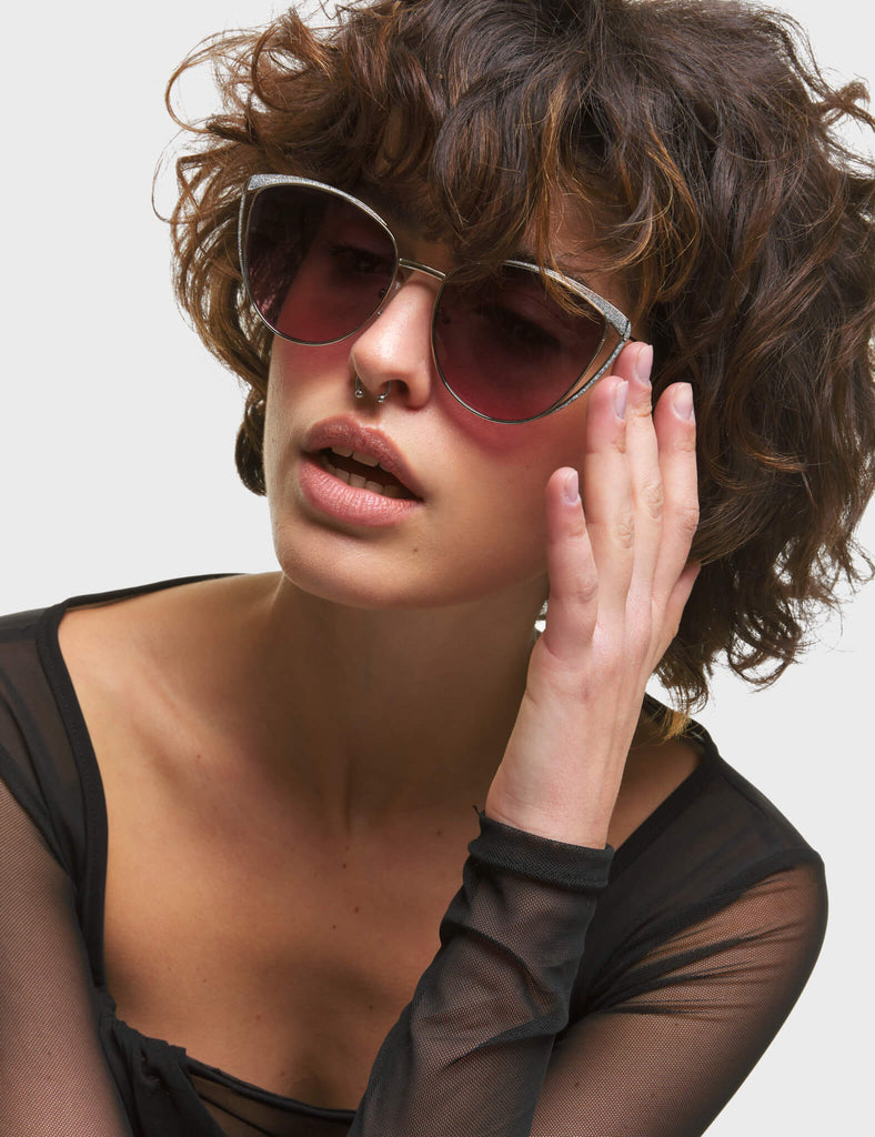 Rosa Cateye Sunglasses. These Cateye sunglasses feature a Silver frame with Silver Glitter eyebrows, and a dark Pink tinted lens.