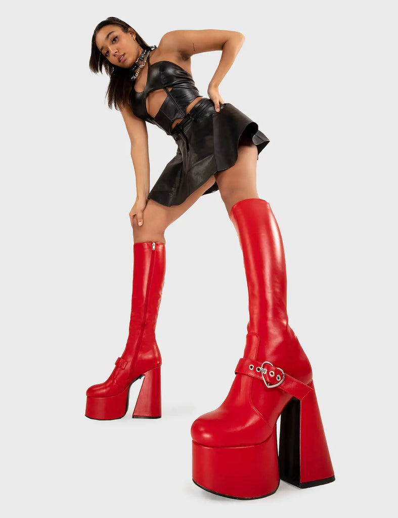 YOU STOLE MY HEART Walk With Love Platform Knee High Boots in Red faux leather. These platform boots feature a minimalist look with a Flared heel, and an adjustable strap. Made with eco-friendly materials and 100% cruelty-free, these platform boots are as ethical as they are chic. - Platform Height - Knee high - Silver heart buckle - Flared heel - High Heel - 100% vegan SKU: LMF 3358 - RedPU
