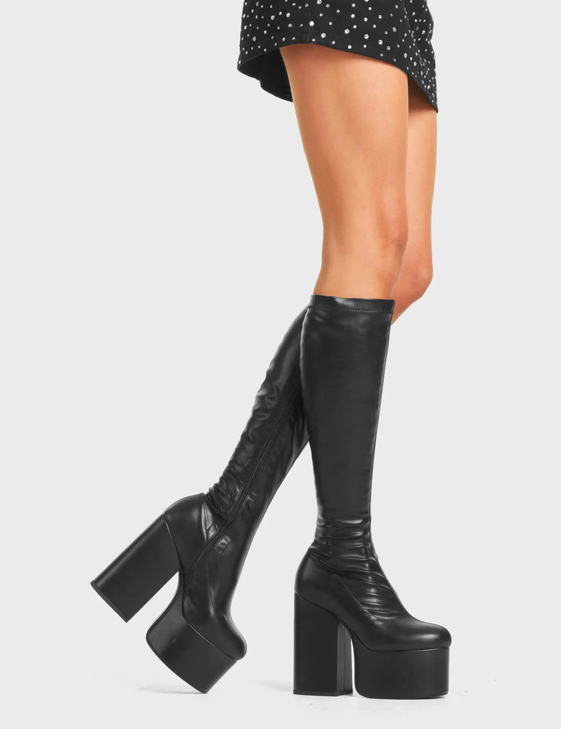 Messenger Platform Knee High Boots in Black faux leather. Feature a minimalist design, platform sole and a stretch fit.